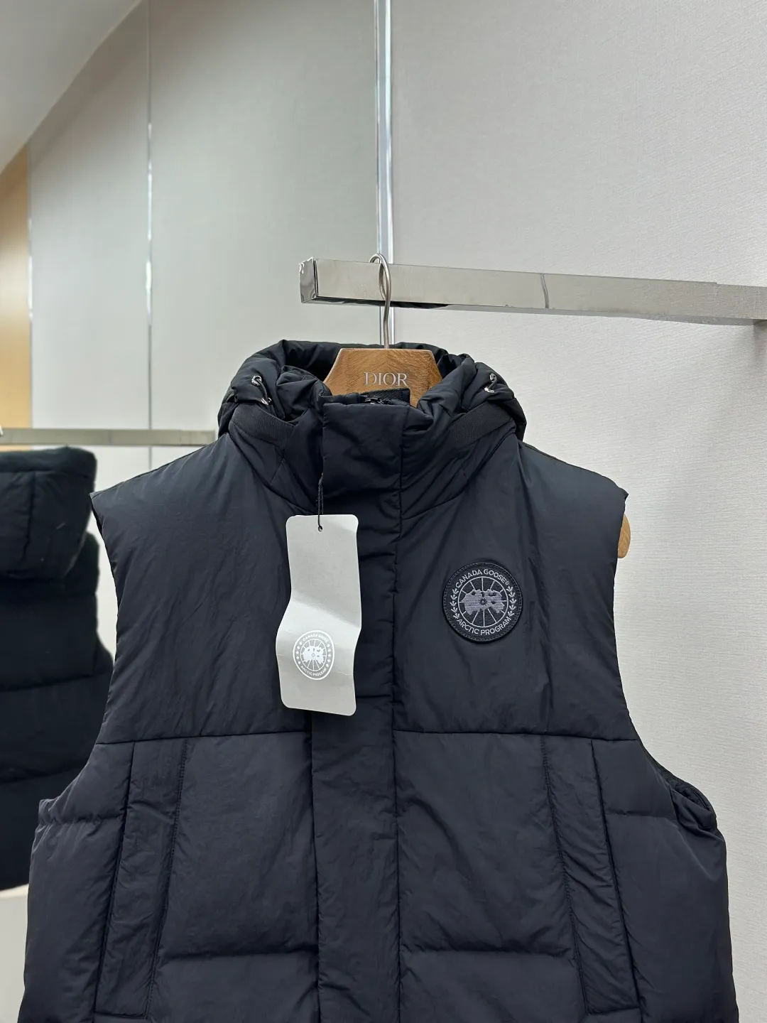 P760 Canada Goose logo hooded down vest Fabric selection: The use of high-quality protective nylon fabric not only enhances the wear resistance of the surface, but also takes into account wind resistance, ensuring excellent performance in various harsh weather conditions.  90 national standard high-quality white duck down: selected high-loft down, weighing 170g, light and warm, with excellent temperature locking performance and good resilience.  Three-dimensional quilting process: Precision thread reinforcement to prevent velvet drilling and ensure that the fluffy and resilient elasticity lasts as new.  Details: Use polyester as the base for woven webbing, and use high-precision computer embroidery to decorate the brand letters on the webbing. The edges of the pattern are clear, the stitches are fine and even, and multiple layers of embroidery threads are stacked to enhance the three-dimensional effect. Accessories: Customized logo Customized zipper pendant Customized hem elastic buckle Customized snap button SIZE: S M L XL